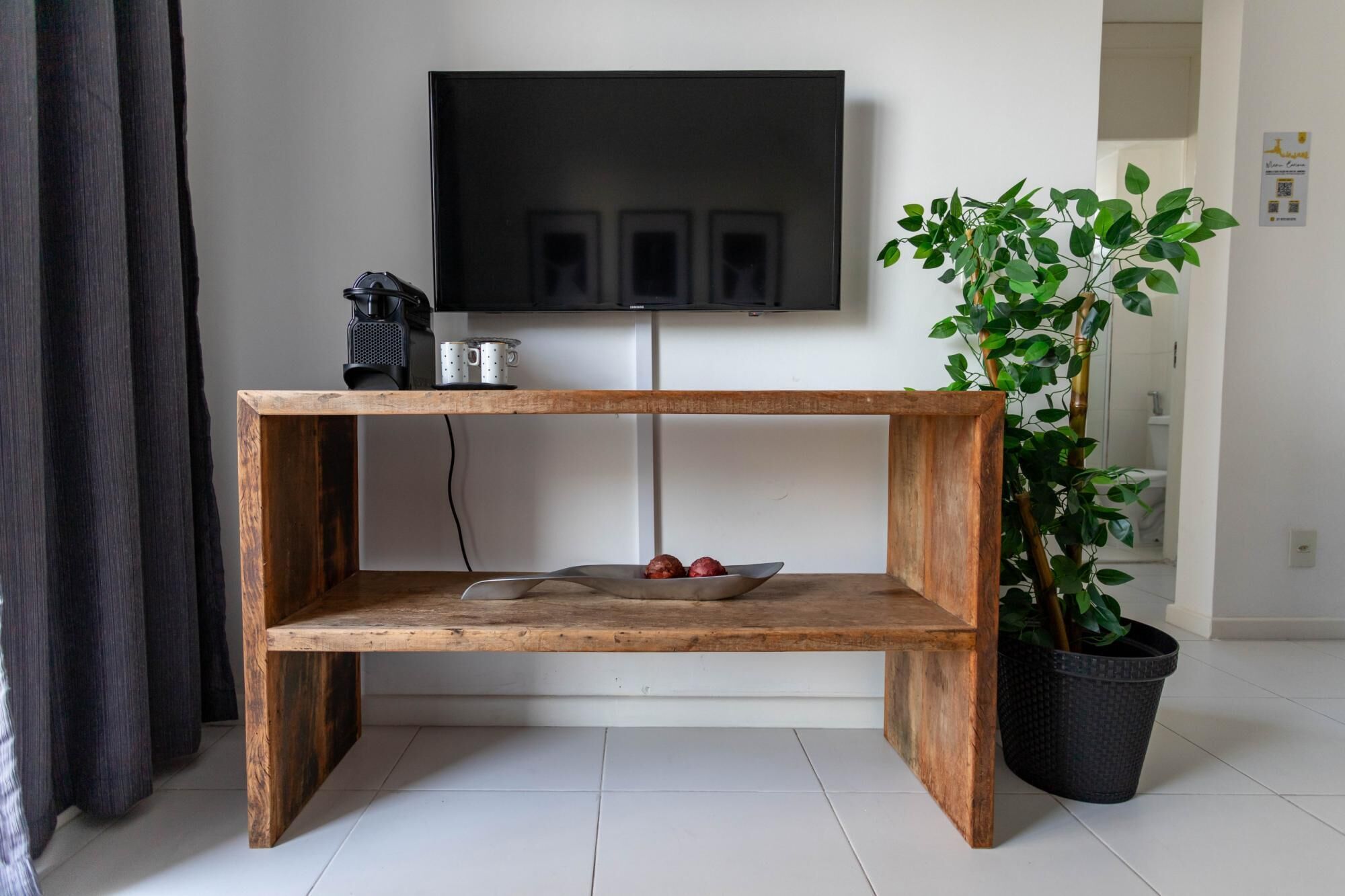 Een houten console tafel met een schaal en twee appels, een potplant en een flatscreen televisie die aan de muur is bevestigd.