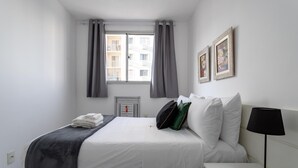A hotel room with a bed, a bedside table, a lamp, a window with curtains, and two framed pictures on the wall. - Charm in Barra da Tijuca Great Wifi Sa508 (Rio de Janeiro)