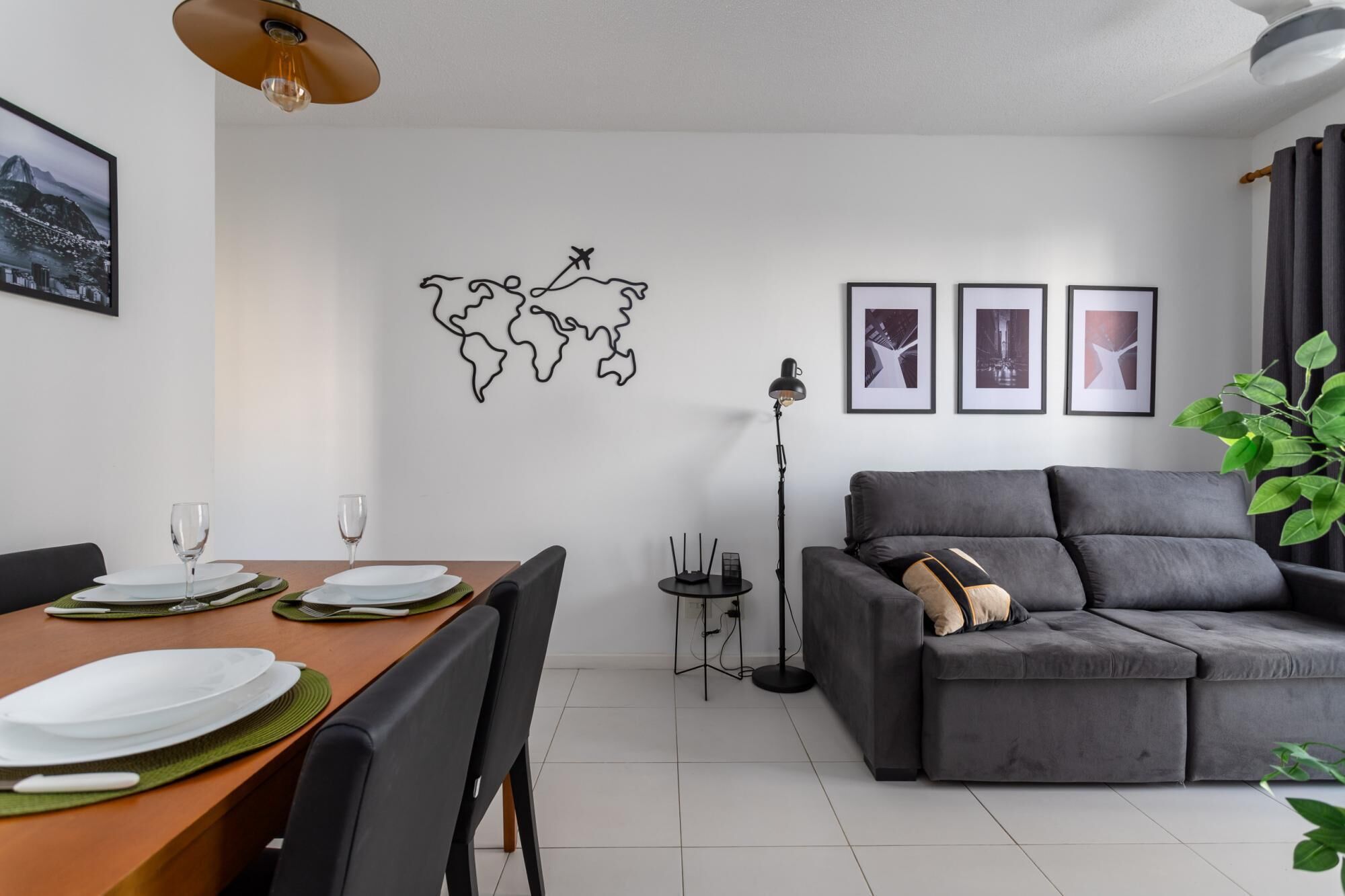 A modern living room with a grey sofa, a dining table set with plates and glasses, a world map artwork, and framed pictures on the wall.
