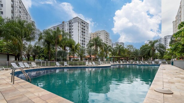 A swimming pool with lounge chairs, surrounded by palm trees and tall buildings. - Charm in Barra da Tijuca Great Wifi Sa508 (Rio de Janeiro)