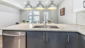 Una cocina con una isla grande, lavavajillas de acero inoxidable, armarios oscuros e iluminación colgante.