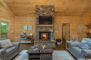 A cozy cabin interior with a stone fireplace, wooden walls, and two grey sofas.