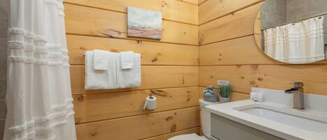 Une salle de bain aux murs lambrissés, équipée de toilettes, d’un lavabo et ornée d’un tableau.