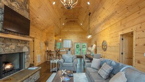 Ein gemütliches Blockhaus-Interieur mit Kamin aus Stein, Holzbalkendecke und einer komfortablen Sitzecke.