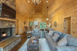 A cozy log cabin interior with a stone fireplace, wooden ceiling, and a comfortable seating area.