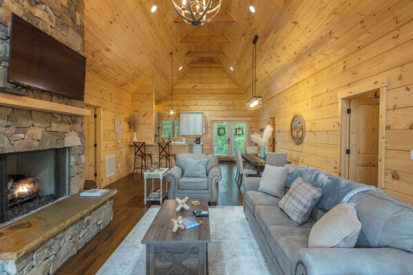A cozy log cabin interior with a stone fireplace, wooden ceiling, and a comfortable seating area.