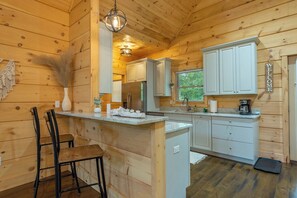 A wooden cabin interior with a kitchen area, including a bar counter, seating, and cabinets. - Dream Mtn~Hot Tub+Fire Pit+Grill~Fireplace & WiFi! (Black Mountain)