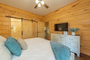 A wooden-paneled room with a bed, a dresser, a television, and a ceiling fan. - Dream Mtn~Hot Tub+Fire Pit+Grill~Fireplace & WiFi! (Black Mountain)