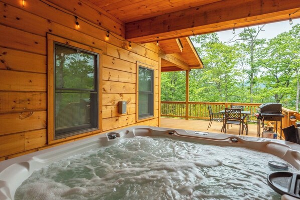 A wooden cabin with a hot tub, outdoor seating, and a view of the surrounding forest. - Dream Mtn~Hot Tub+Fire Pit+Grill~Fireplace & WiFi! (Black Mountain)