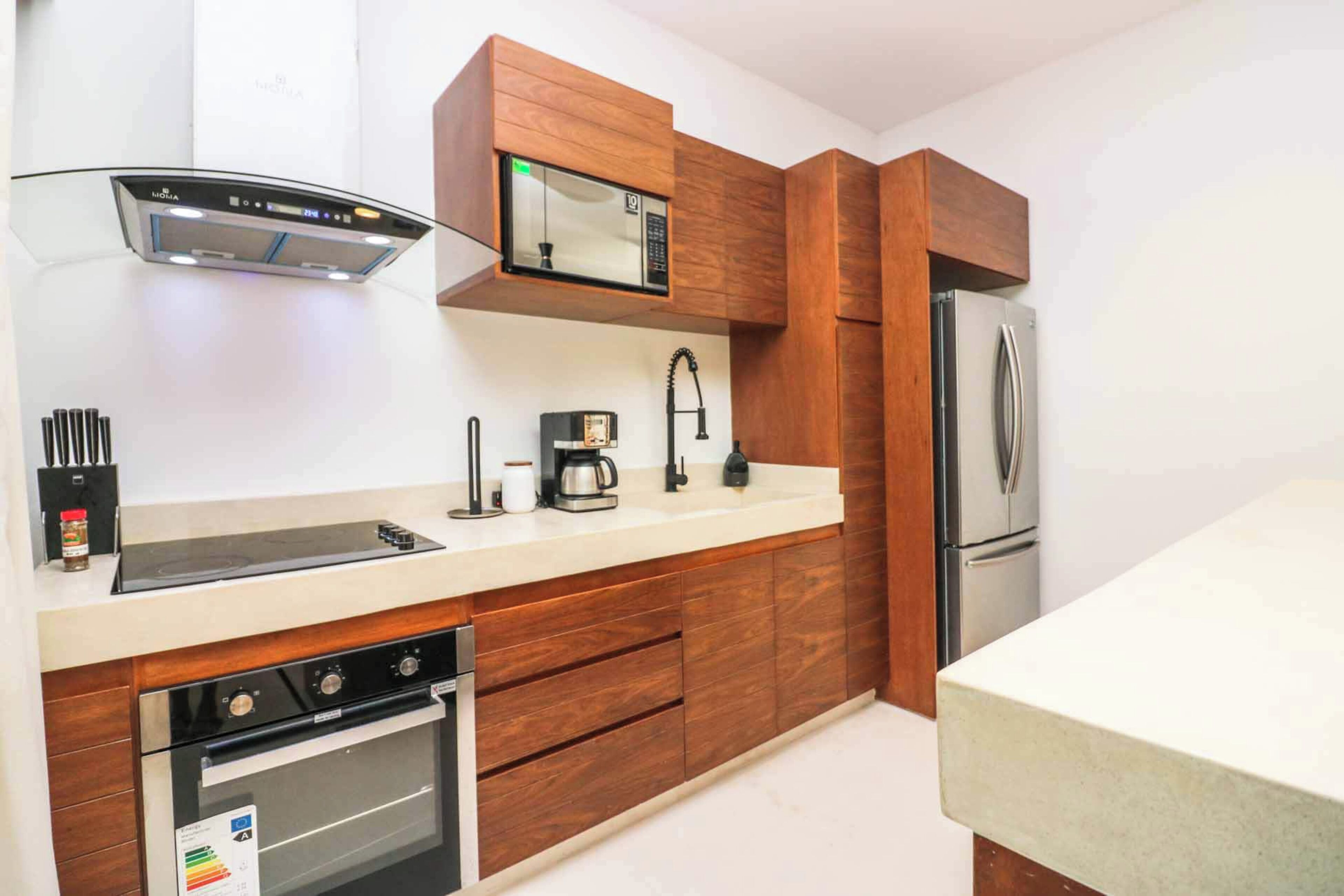 A modern kitchen with wooden cabinets, a built-in microwave, a stainless steel refrigerator, and a stove.