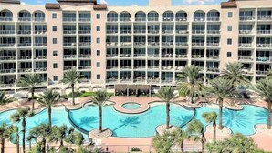 Un hotel de varios pisos con una amplia piscina central rodeada de palmeras.