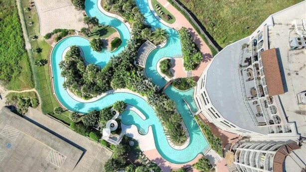Vista aérea de un resort con piscina sinuosa, exuberante vegetación y un edificio de techo curvo.