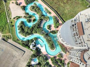 Una vista aerea di un resort con una piscina sinuosa, una vegetazione rigogliosa e un edificio con un tetto curvo.