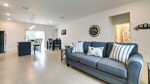 A modern living room with a grey sofa, a dining area with a table and chairs, and a kitchen area with a fridge and cabinets. - Bright, Pet-Friendly Home: 16 Mi to Downtown Ocala (Ocala)