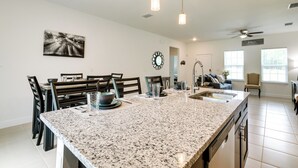 A spacious kitchen with a granite island, modern pendant lights, and a dining area with dark wooden chairs and a white tablecloth. - Bright, Pet-Friendly Home: 16 Mi to Downtown Ocala (Ocala)