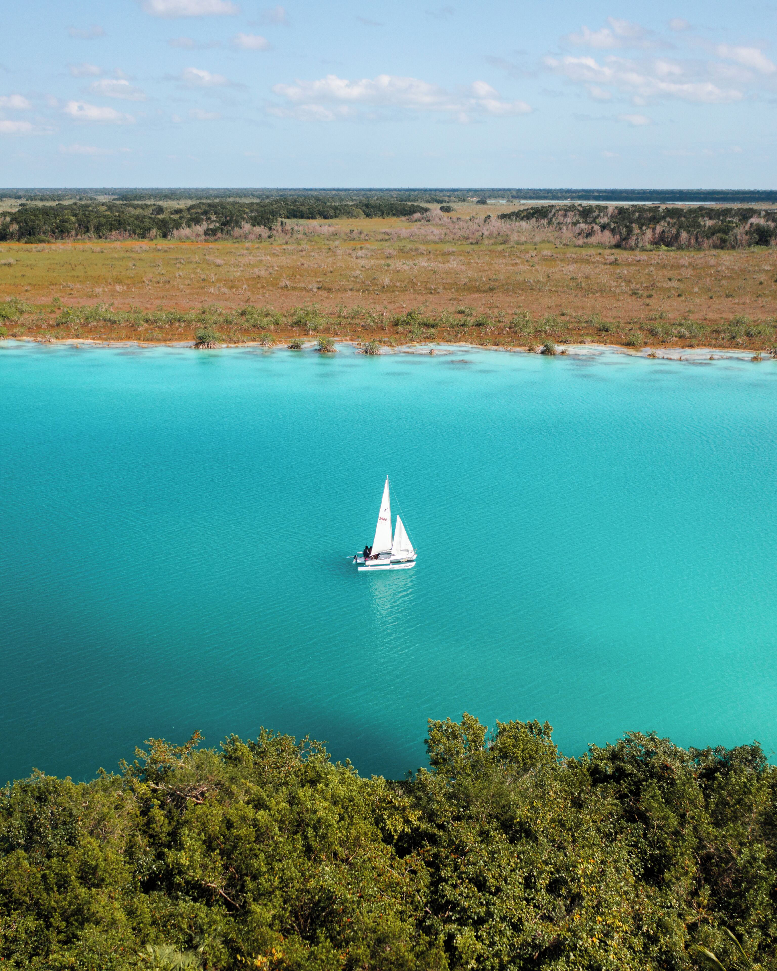 A sailboat on a turquoise sea with a forested shoreline.