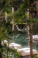Una hamaca sobre una piscina, con sillones de descanso, rodeada de follaje.