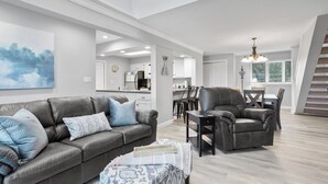 Un salon moderne avec un canapé en cuir gris, un fauteuil assorti et un coin repas agrémenté d’un lustre.