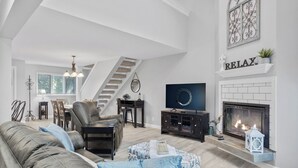 Un salon spacieux doté d’une cheminée, d’un téléviseur et d’un escalier menant à un autre niveau.