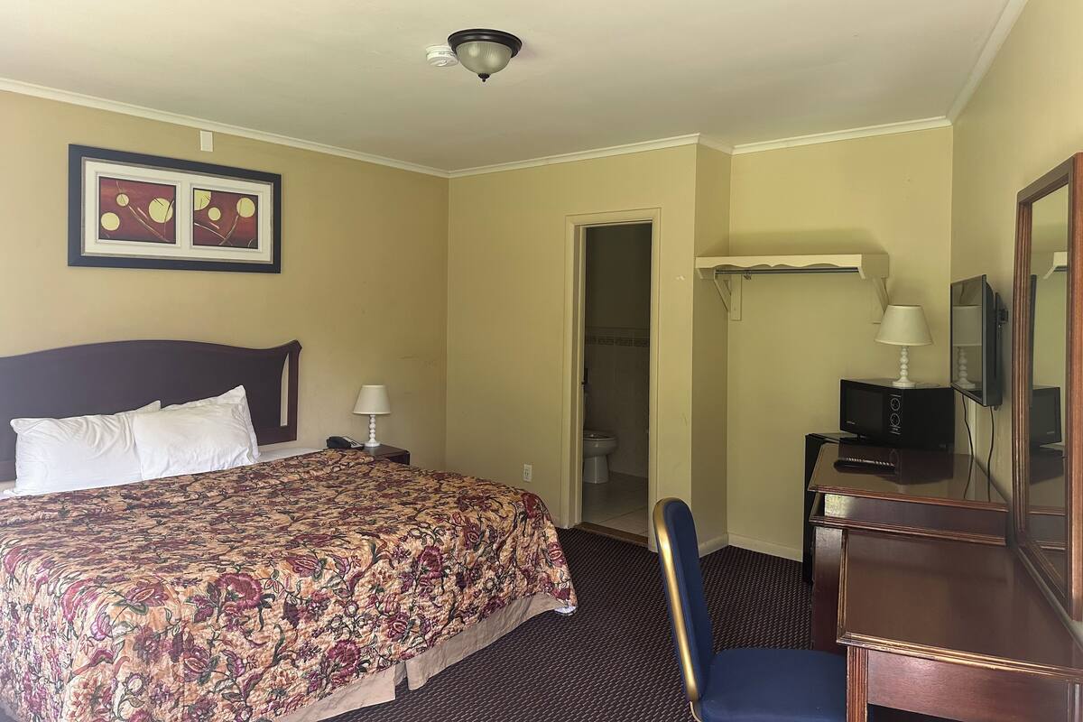 A hotel room with a bed, a desk, a chair, a television, and a door leading to a bathroom.