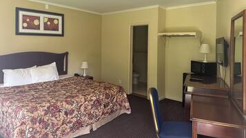 A hotel room with a bed, a desk, a chair, a television, and a door leading to a bathroom.