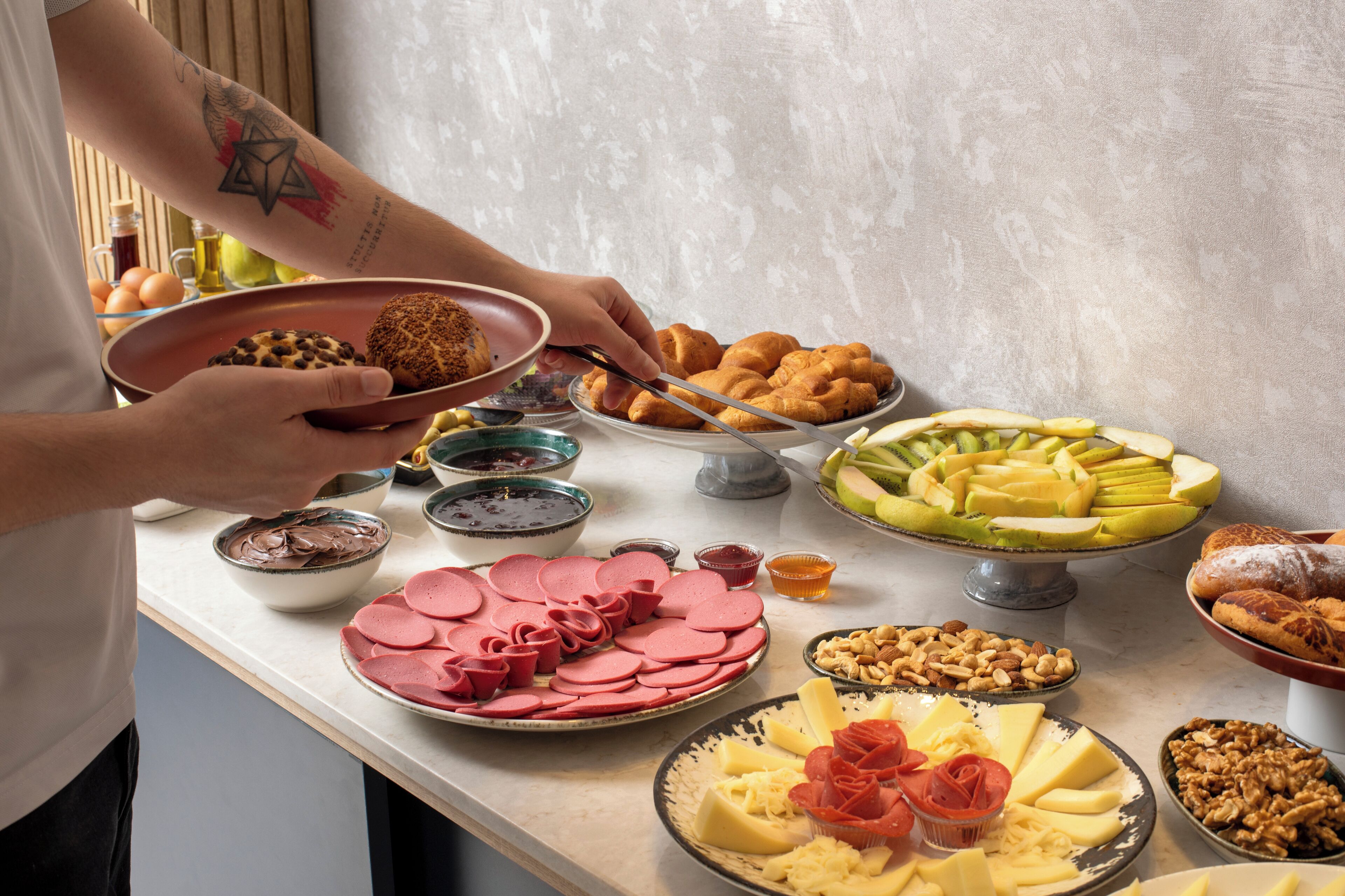 Uma mesa de buffet com diversos alimentos, incluindo carnes fatiadas, queijos, frutas e nozes.