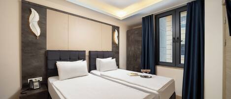 A hotel room with two beds, a dark headboard, a wall-mounted phone, and a window with curtains.
