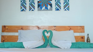 Una cama bien hecha con cabecera de madera, almohadas blancas y toallas verdes dispuestas en forma de corazón.