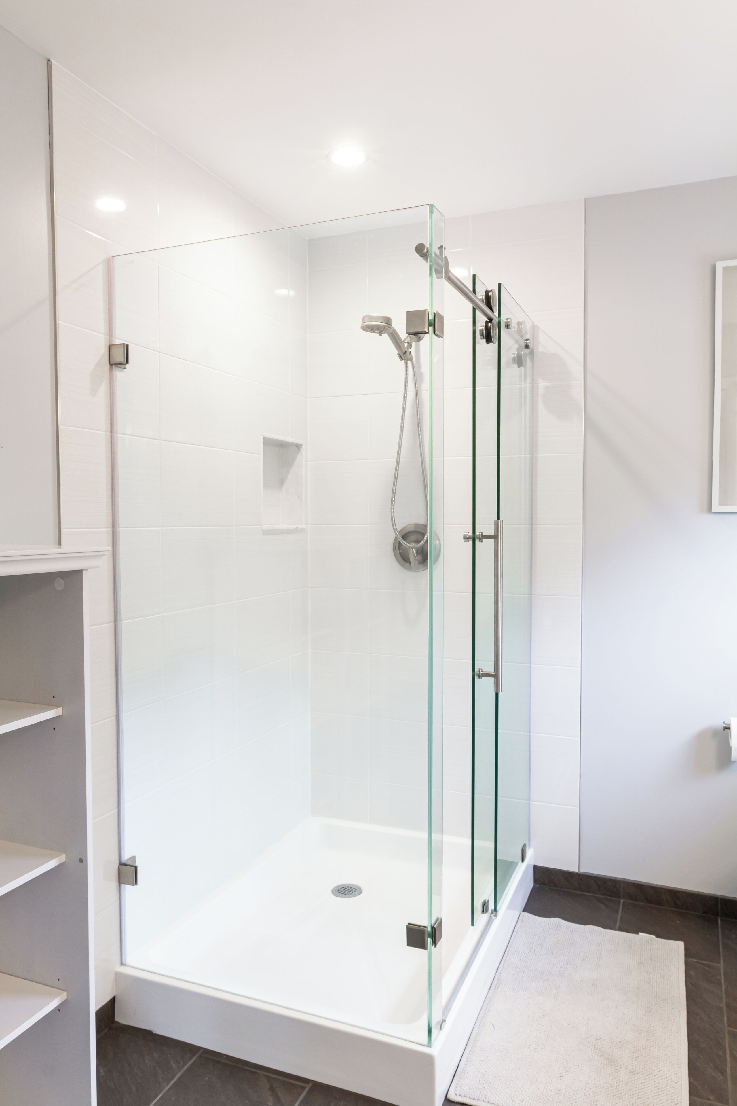 A modern bathroom with a glass-enclosed shower, white tiled walls, and a white floor.