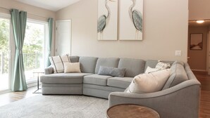 Uma sala de estar moderna com um sofá modular cinzento, uma mesa de centro redonda e duas pinturas de pássaros penduradas na parede.