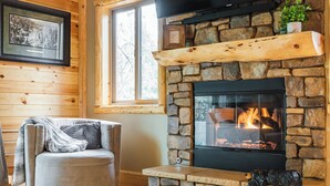 A cozy cabin interior with a stone fireplace, a comfortable armchair, and a framed picture on the wall. - SNOW BUNNY - Game Room - Hot Tub - Fire Pit (Big Bear Lake)