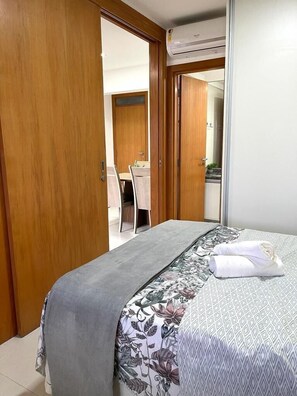 A bedroom with a bed, a wooden wardrobe, a bathroom with a shower, and a dining area with a table and chairs.