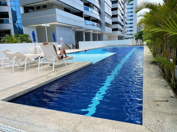 A swimming pool with lounge chairs and a building in the background.