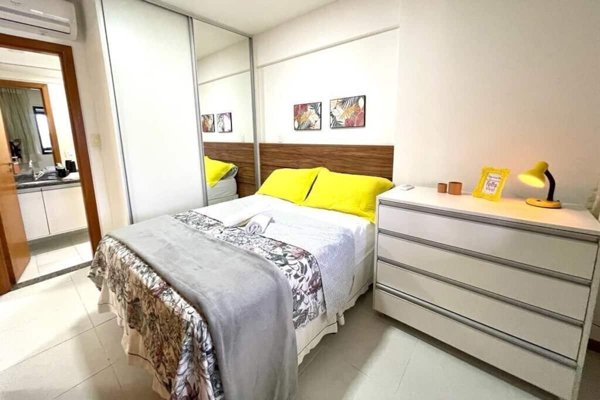 A bedroom with a bed, bedside table, dresser, and a mirror.
