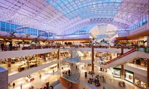 A multi-level shopping mall with a glass ceiling, escalators, and various retail stores.