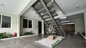 Un interior espacioso con una escalera moderna, un pequeño jardín con un árbol y un extintor.