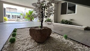 Una orquídea blanca en maceta sobre una superficie de guijarros, con vista a un edificio y una ventana al fondo.