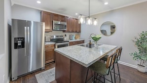 A modern kitchen with stainless steel appliances, wooden cabinets, a granite countertop, and a bar stool. - Outdoorsy ~ Fresh Spring Vibes ~ Sauna & Cold Plunge ~ 10min Downtown (Raleigh)