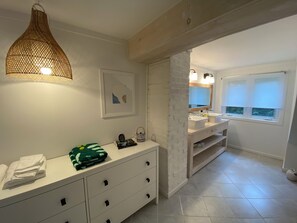 A modern bathroom with a white vanity, a hanging light fixture, a framed artwork, and a window with blinds. - Muskoka Zen, Outdoor Jacuzzi Spa, Ski or Hike 3 Bedroom 2 Bath (Huntsville)