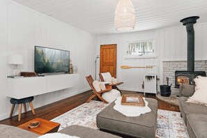 A cozy living room with a television, a fireplace, a wooden chair, and a sofa. - Muskoka Zen, Outdoor Jacuzzi Spa, Ski or Hike 3 Bedroom 2 Bath (Huntsville)