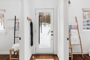 A white door with a view of a snowy landscape, a wooden ladder, and a chair with a towel.