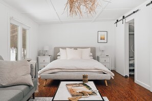 Quarto moderno com cama, mesas de cabeceira, penteadeira, uma cadeira, mesa de centro e luminária suspensa.