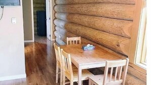 A wooden dining table with four chairs, a ceiling light fixture, and a wooden wall with a log pattern.