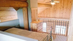 A bedroom with a wooden ceiling, a bed, a dresser, and a window with a view.