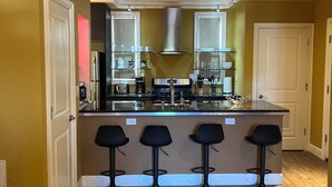 A kitchen with a central island, bar stools, and a stainless steel range hood.