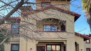 A two-story house with a beige facade, red trim, and a front entrance with a glass door.