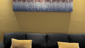 A modern living room with a dark gray sofa, two beige throw pillows, and a large abstract painting on the wall.