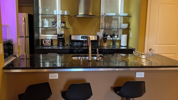 A kitchen with a central island, bar stools, a stainless steel refrigerator, and a range hood.