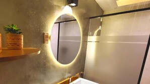 A modern bathroom with a round mirror, a white sink, and a shower area. - Sun Backpackers (Quito)