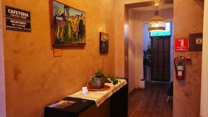 A hallway with a coffee shop sign, a painting, a fire extinguisher, and a plant on a table. - Sun Backpackers (Quito)